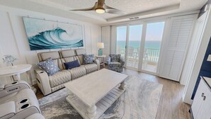 Een ruime woonkamer met een groot raam met uitzicht op de oceaan, een plafondventilator en een gezellige zithoek.