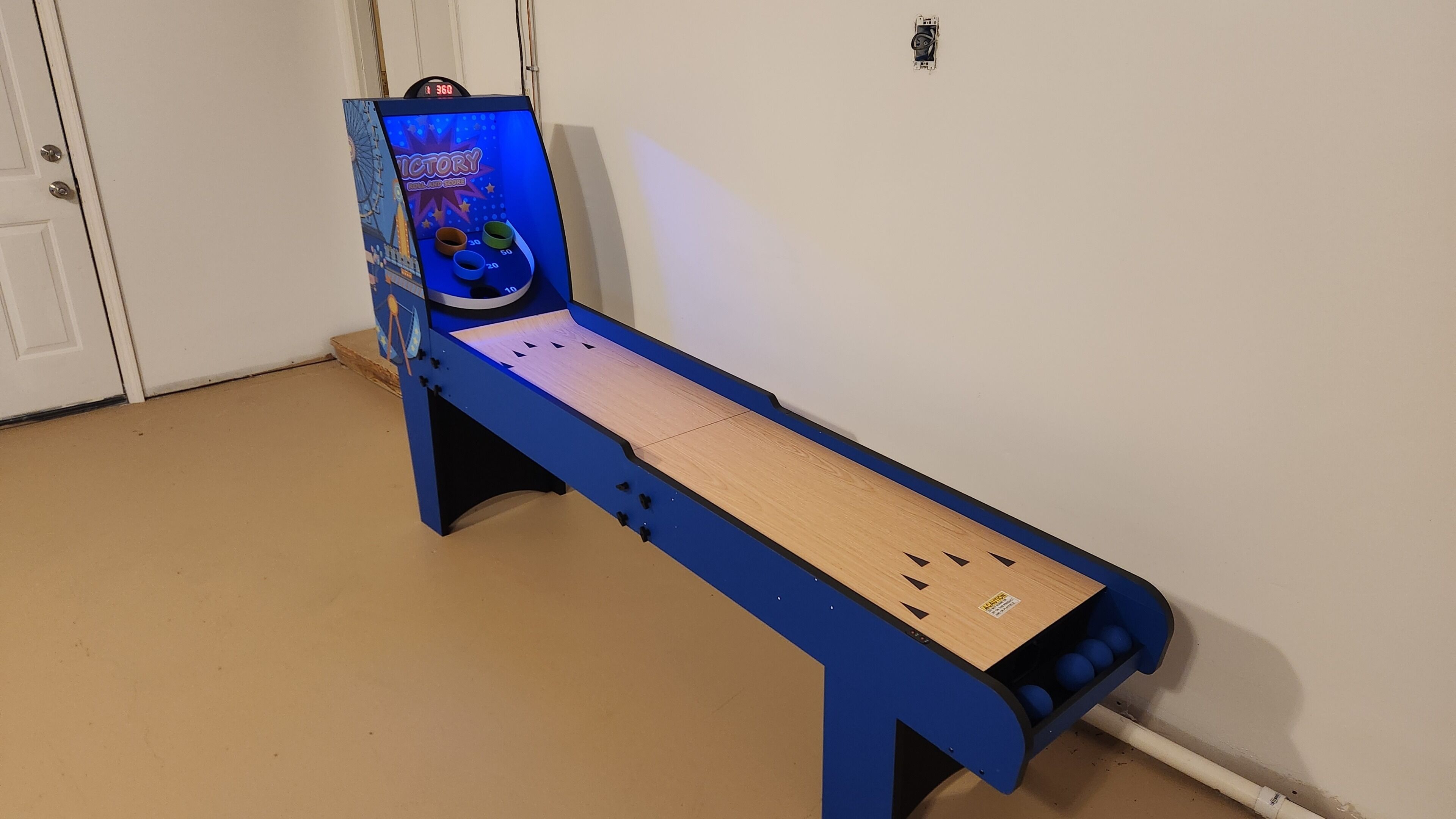 Une table de baby-foot bleue, dotée d’un tableau de score numérique, et une table en bois placée devant.