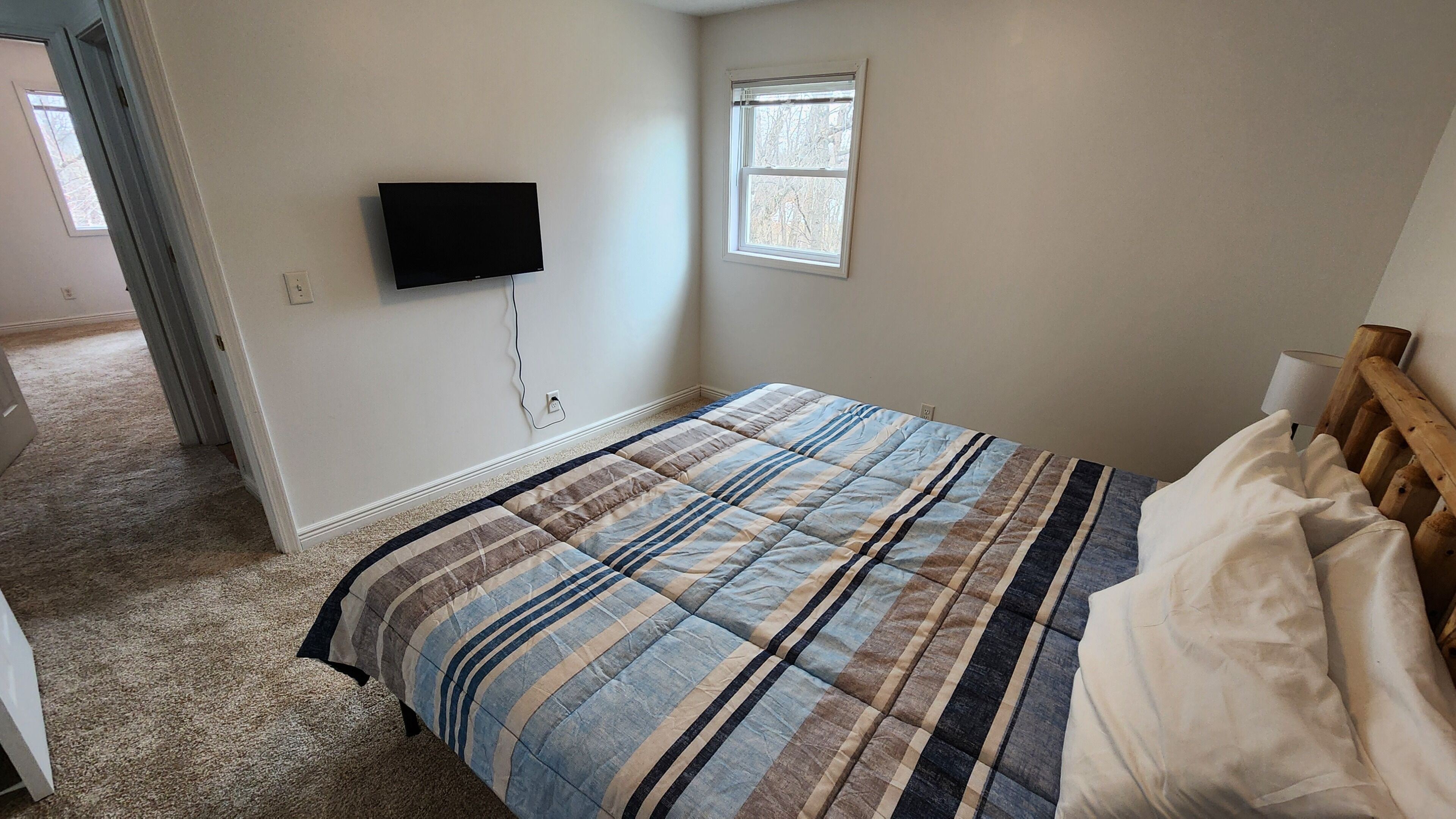 A bedroom with a bed, a television mounted on the wall, and a window.