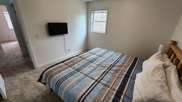 A bedroom with a bed, a television mounted on the wall, and a window.