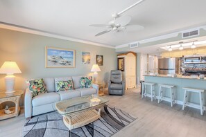 A living room with a sofa, a glass coffee table, a chair, a lamp, and a painting on the wall. - 🌊Beachfront with Great Amenities | Stunning Views | Gateway Villas 595🌊 (Fort Myers Beach)