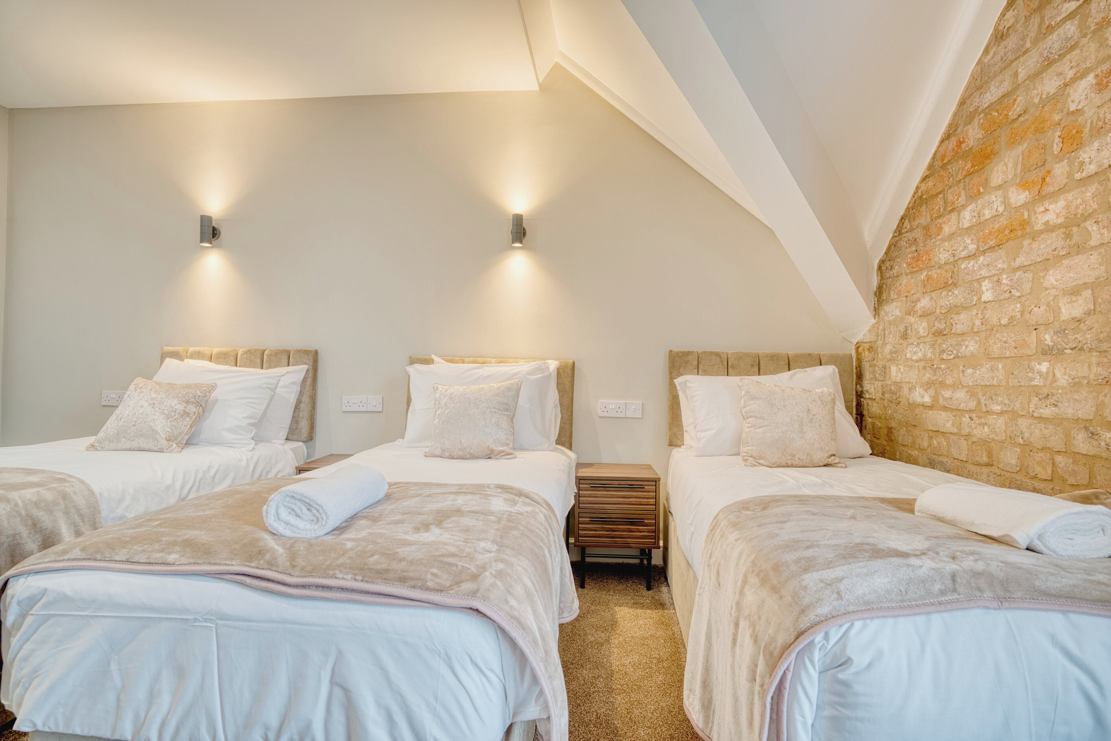 Habitación de hotel con tres camas, una pared de ladrillo e iluminación empotrada.