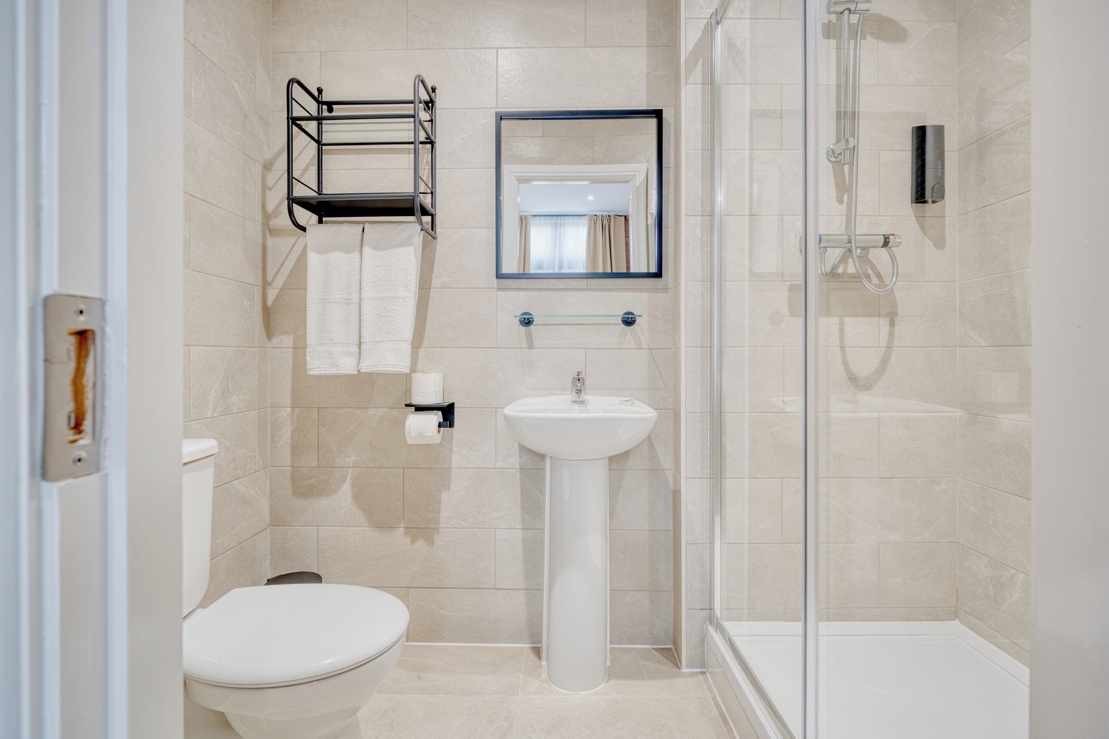 A bathroom with a toilet, sink, shower, towel rack, and mirror.