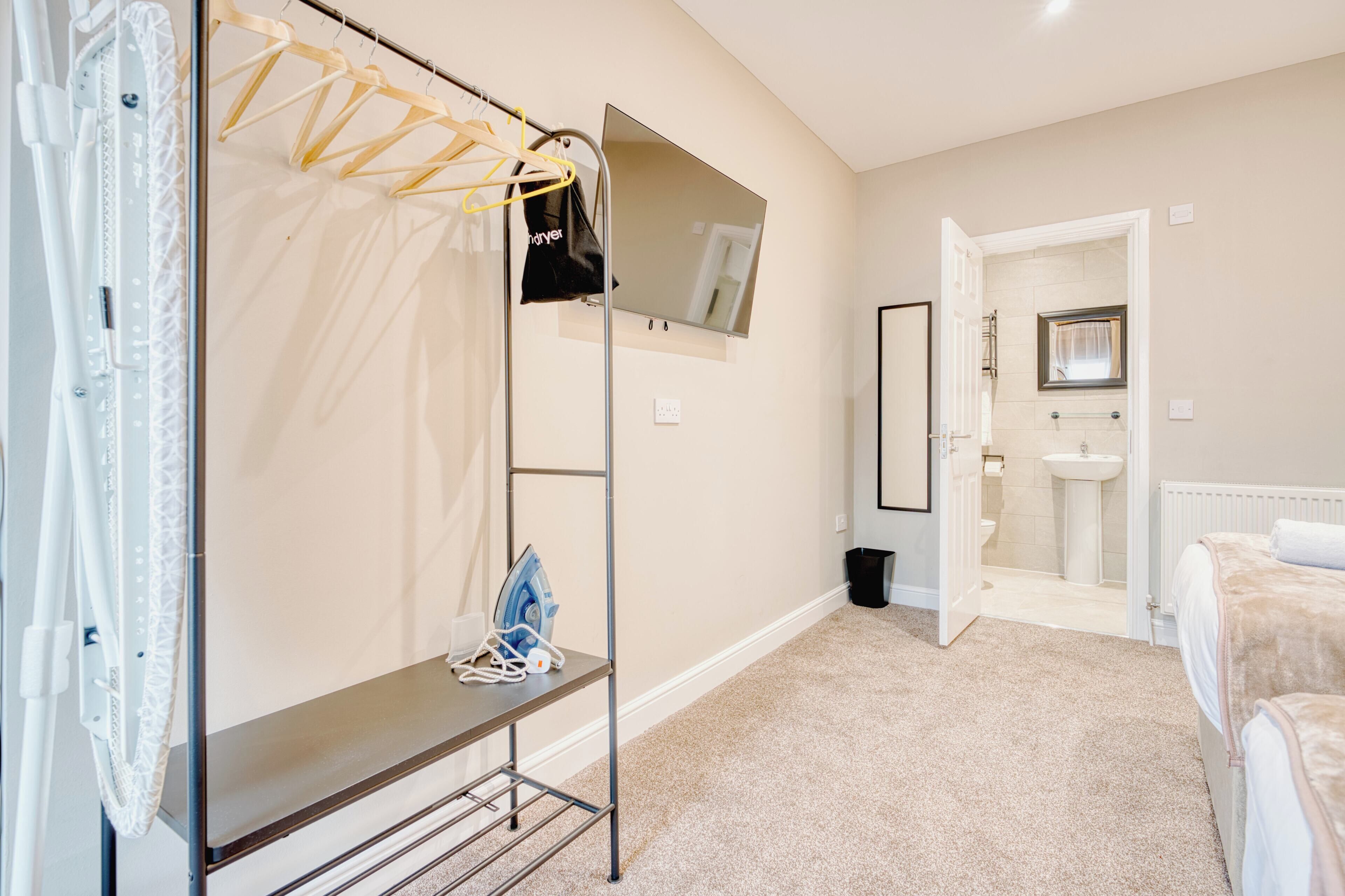 Ein Schlafzimmer mit Bett, Nachttisch, Kleiderstange, Spiegel, Bad mit Waschbecken und Toilette sowie einer Duschkabine.