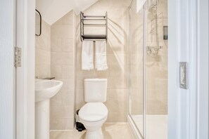 Egy modern fürőszoba, amelyben WC, mosdókagyló és üvegfalas zuhanyzó található.