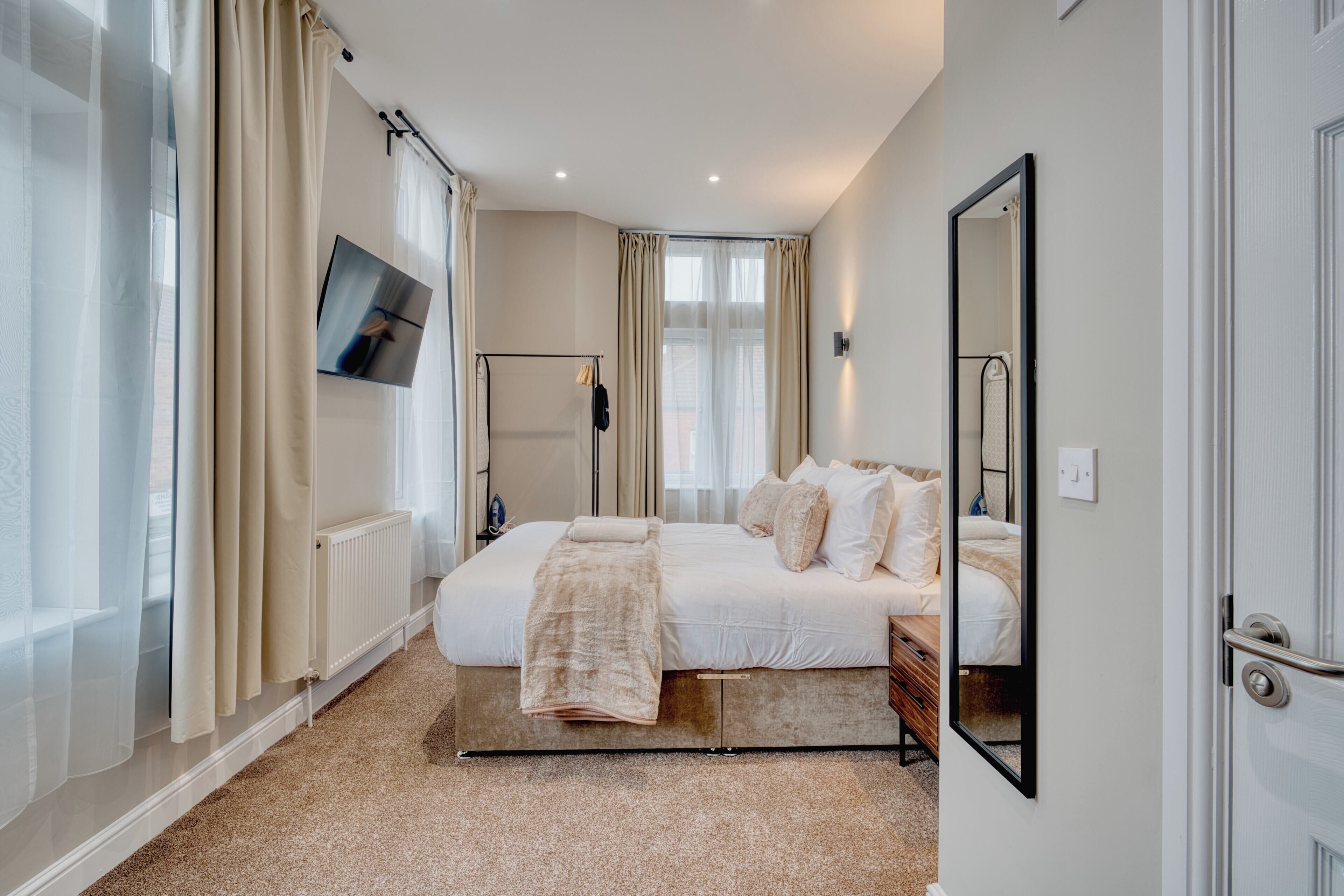 Une chambre à coucher avec un grand lit, un téléviseur fixé au mur, un miroir et un radiateur.