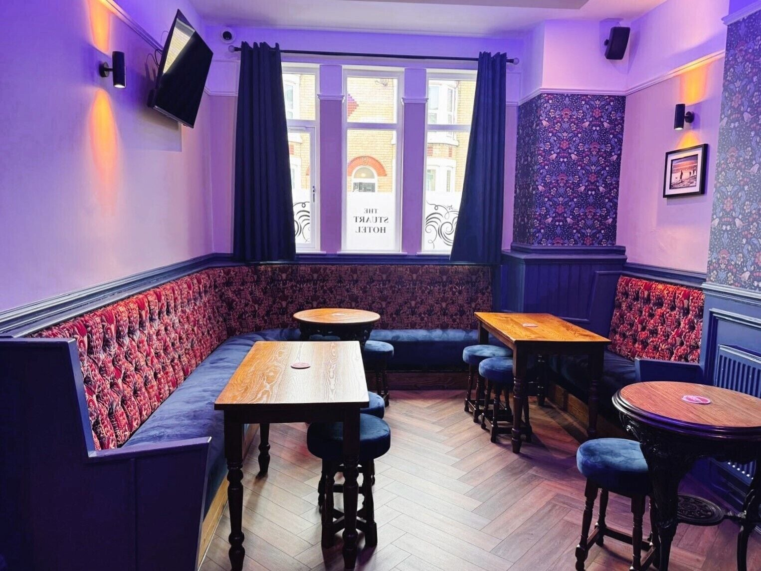 A room with a corner booth seating area, wooden tables, and a patterned wall.