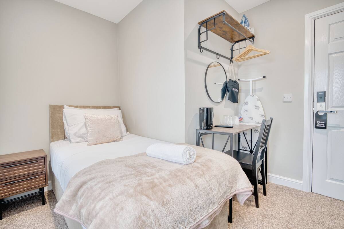 A bedroom with a bed, a desk with a chair, a hanging clothes rack, and a door.