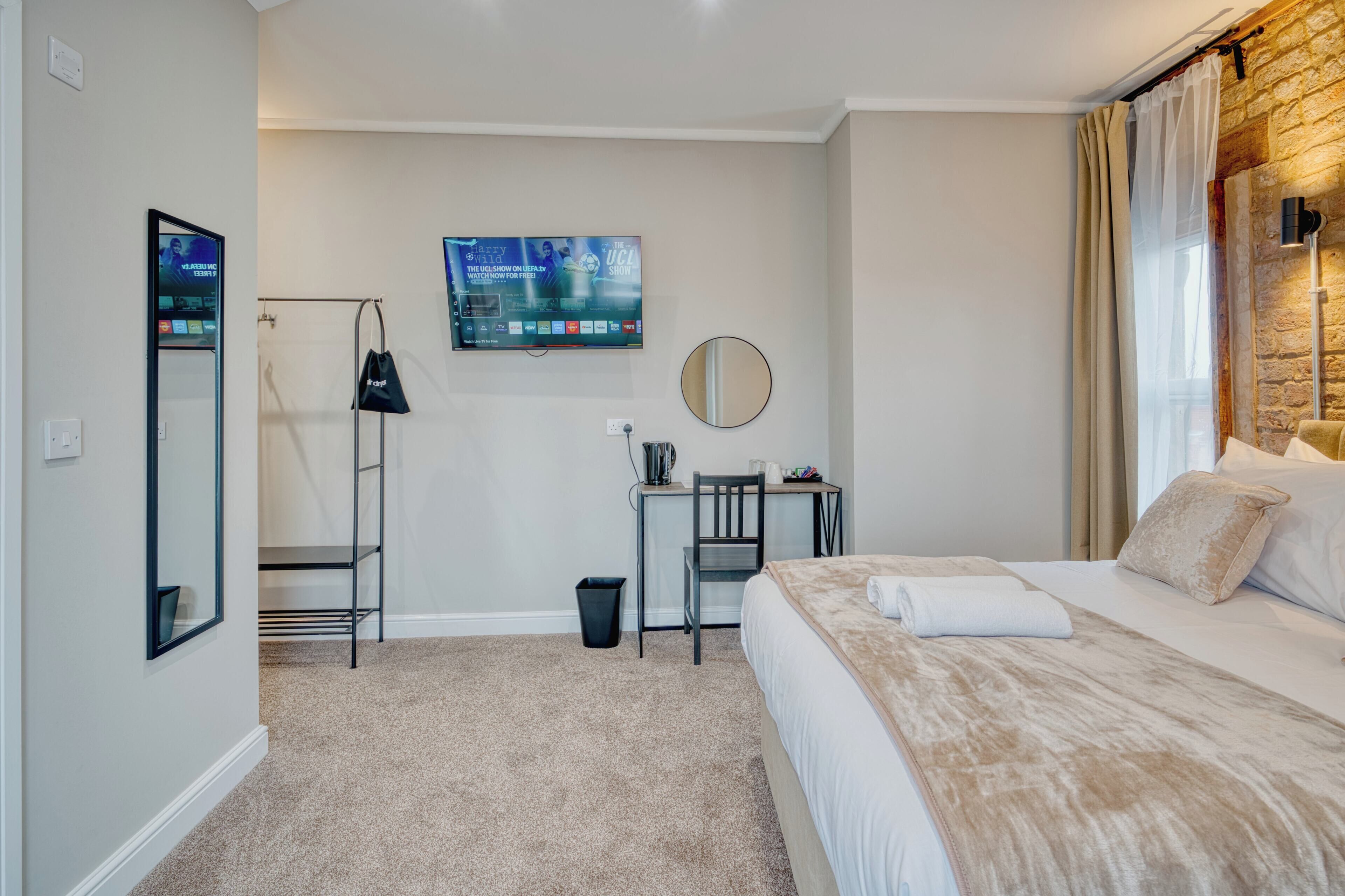 A hotel room with a bed, a desk, a chair, a TV, a mirror, and a trash bin.