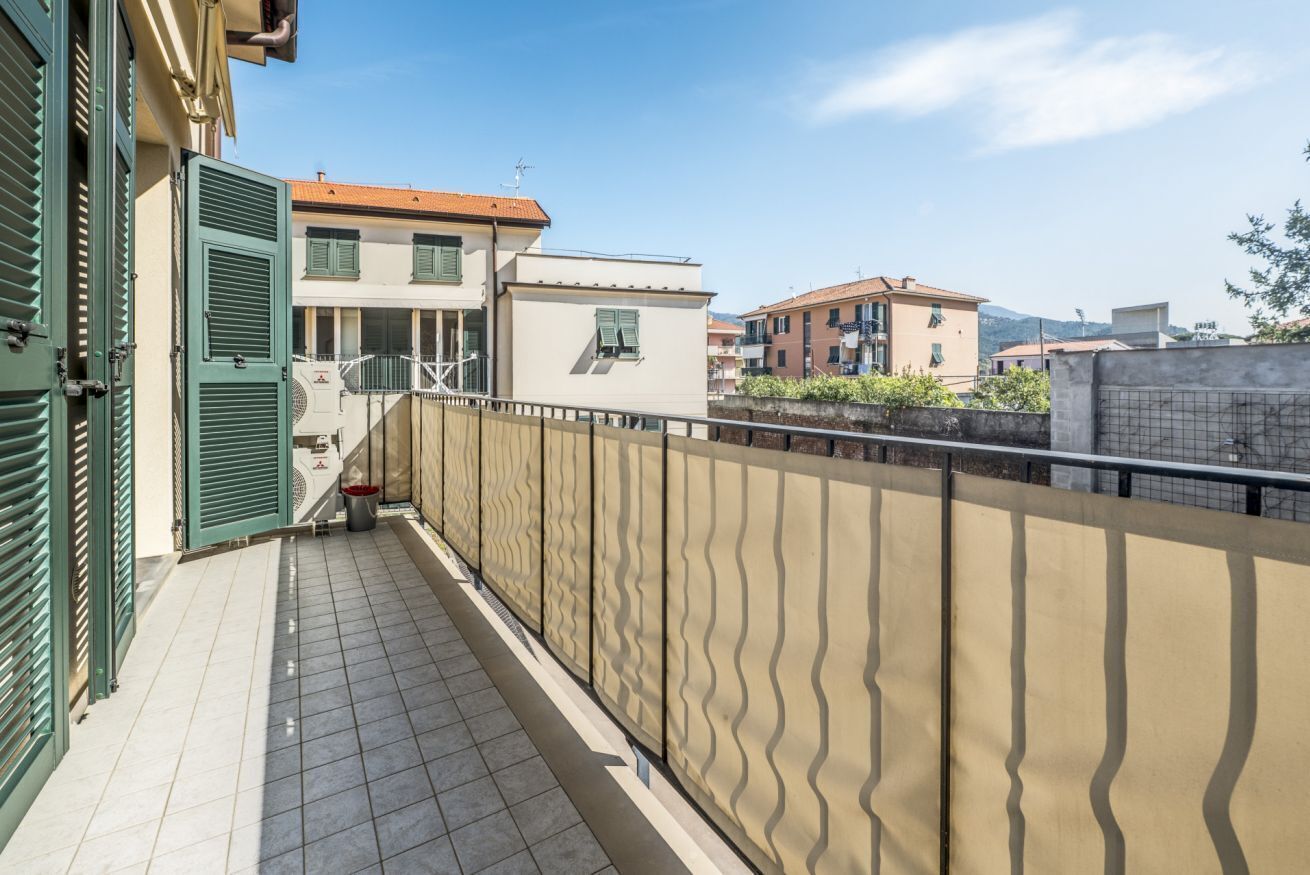 Un balcone con ringhiera ondulata, pavimento piastrellato e un edificio con tetto rosso sullo sfondo.