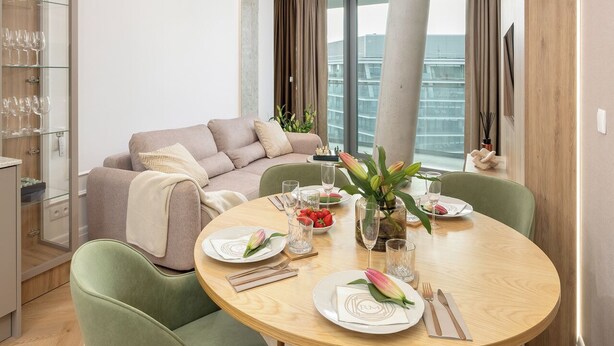 Uma área de jantar moderna com uma mesa redonda, cadeiras estofadas em verde e uma luminária pendente diferenciada.