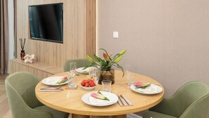 Uma área de refeições com uma mesa redonda, cadeiras verdes, uma televisão de tela plana na parede e um lustre.