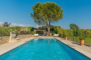 Una piscina con sillas de descanso, una pérgola y un árbol grande.