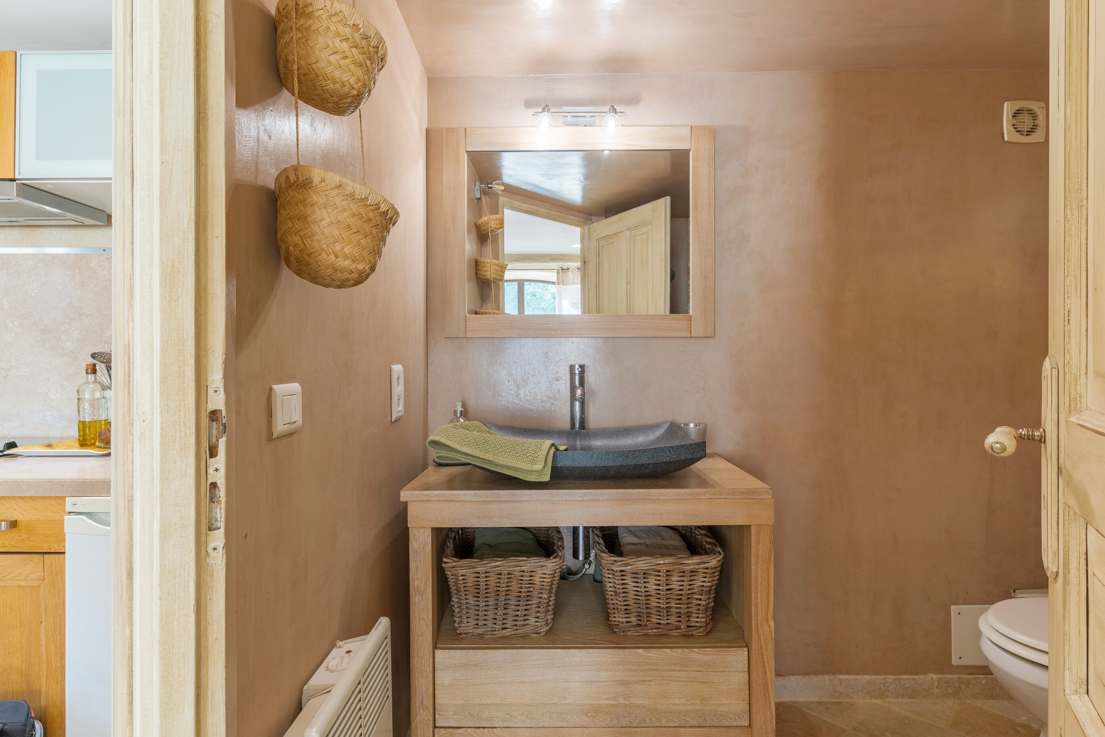 Ein Badezimmer mit einem Holzwaschtisch, einem Spiegel, Korbwäschekörben und einer Toilette.