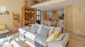 A spacious living room with a sofa, a wooden bookshelf, and a dining area. - Les Olivandes Cottage with Pool (Saint-Cannat)
