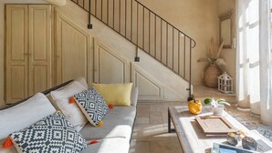 A staircase with a metal railing, a sofa with patterned cushions, a small table with decorative items, and a window with curtains. - Les Olivandes Cottage with Pool (Saint-Cannat)