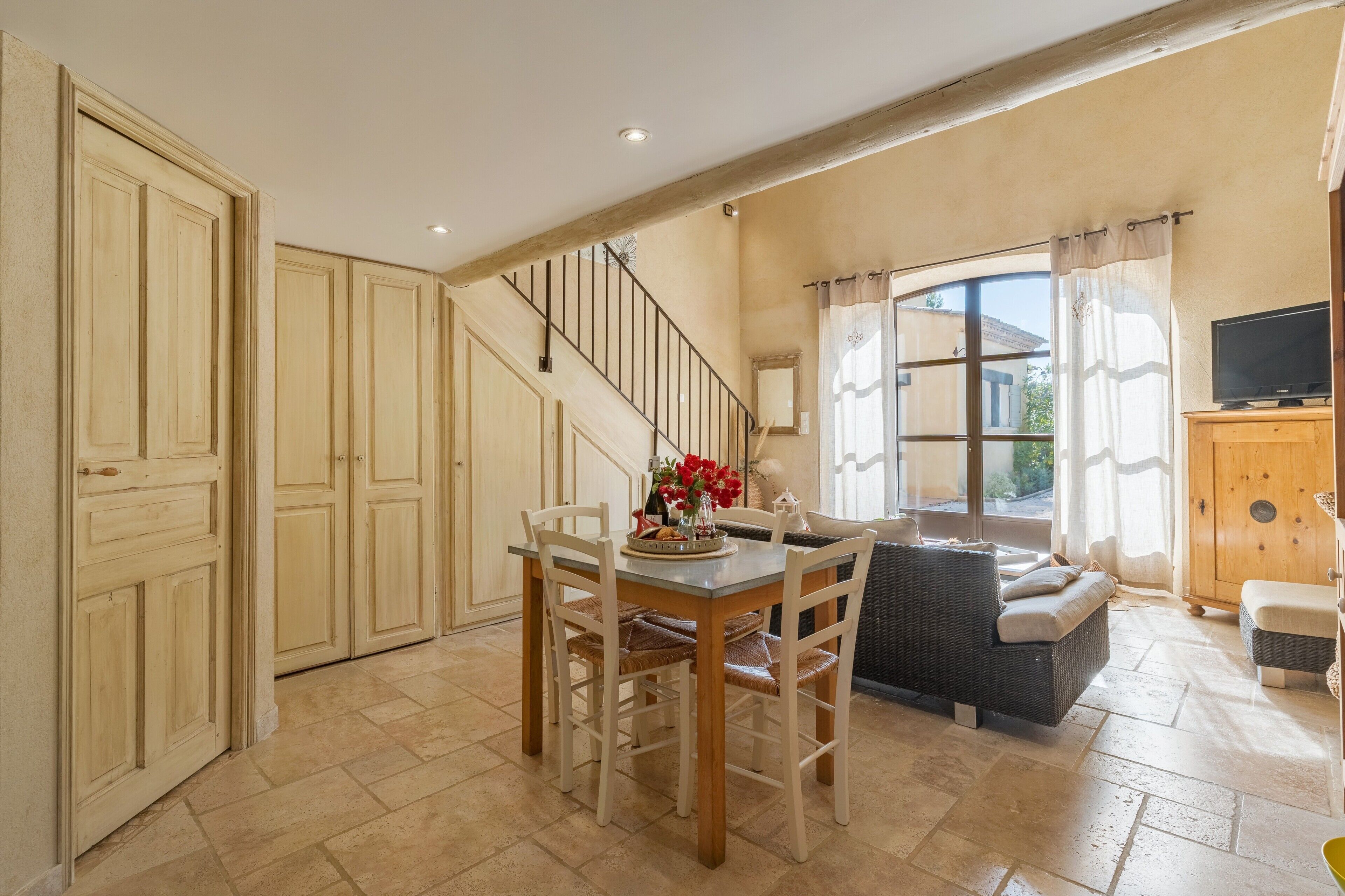 A spacious living area with a dining table, chairs, a sofa, a staircase, and a television.