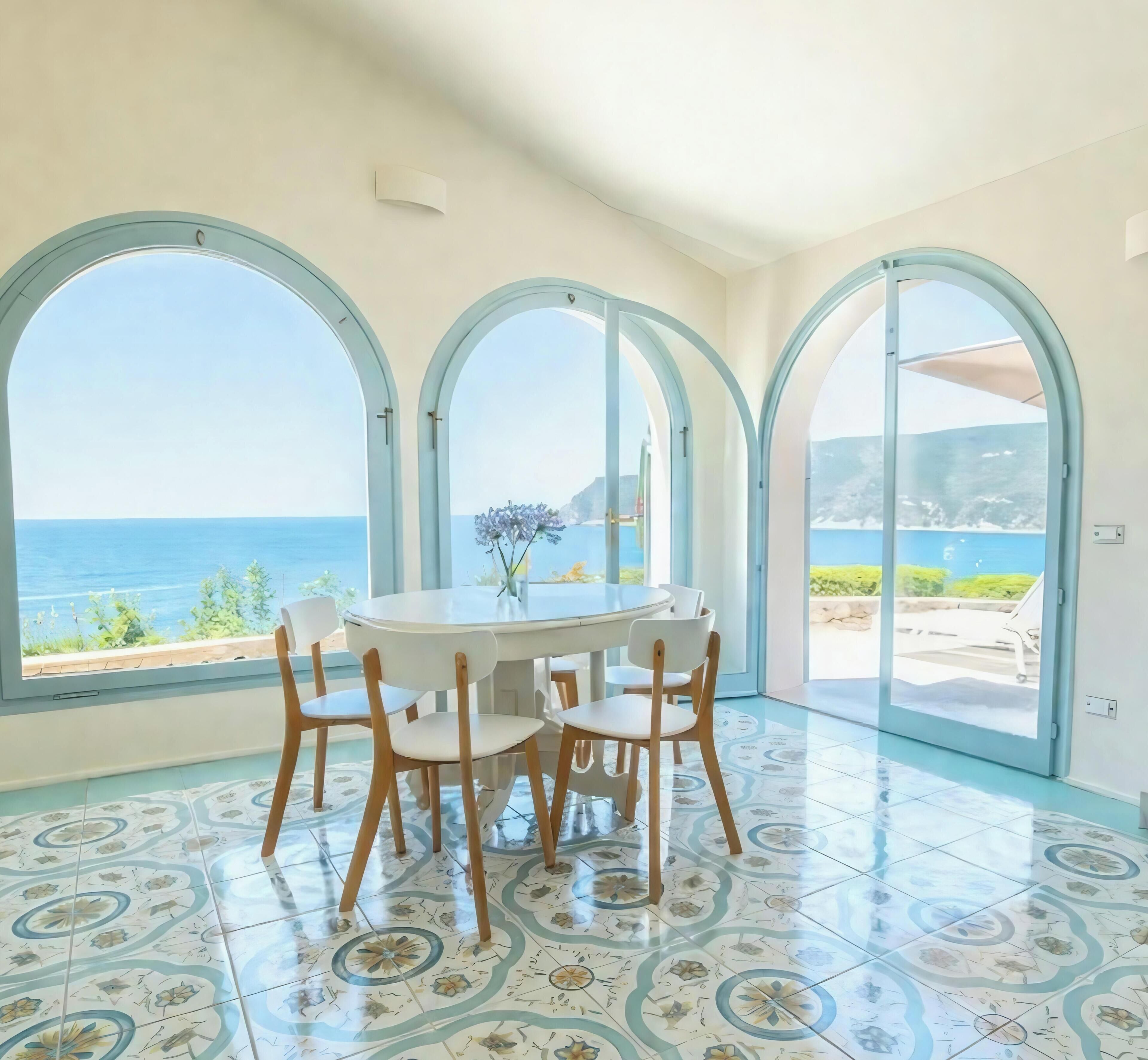 Comedor con una mesa redonda y sillas, ventanas arqueadas grandes y baldosas con diseño.