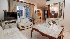 A living room with a sofa, a TV, a dining table, and a kitchen in the background.