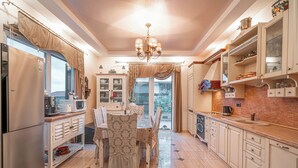 A kitchen with a dining table, chairs, a refrigerator, cabinets, and a chandelier.