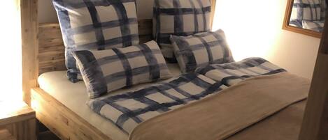 A wooden bed with checkered bedding, a nightstand, a painting on the wall, and a mirror.