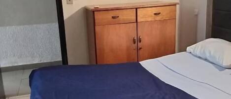 Un dormitorio con una cama, un aparador de madera, un espejo redondo y una puerta.