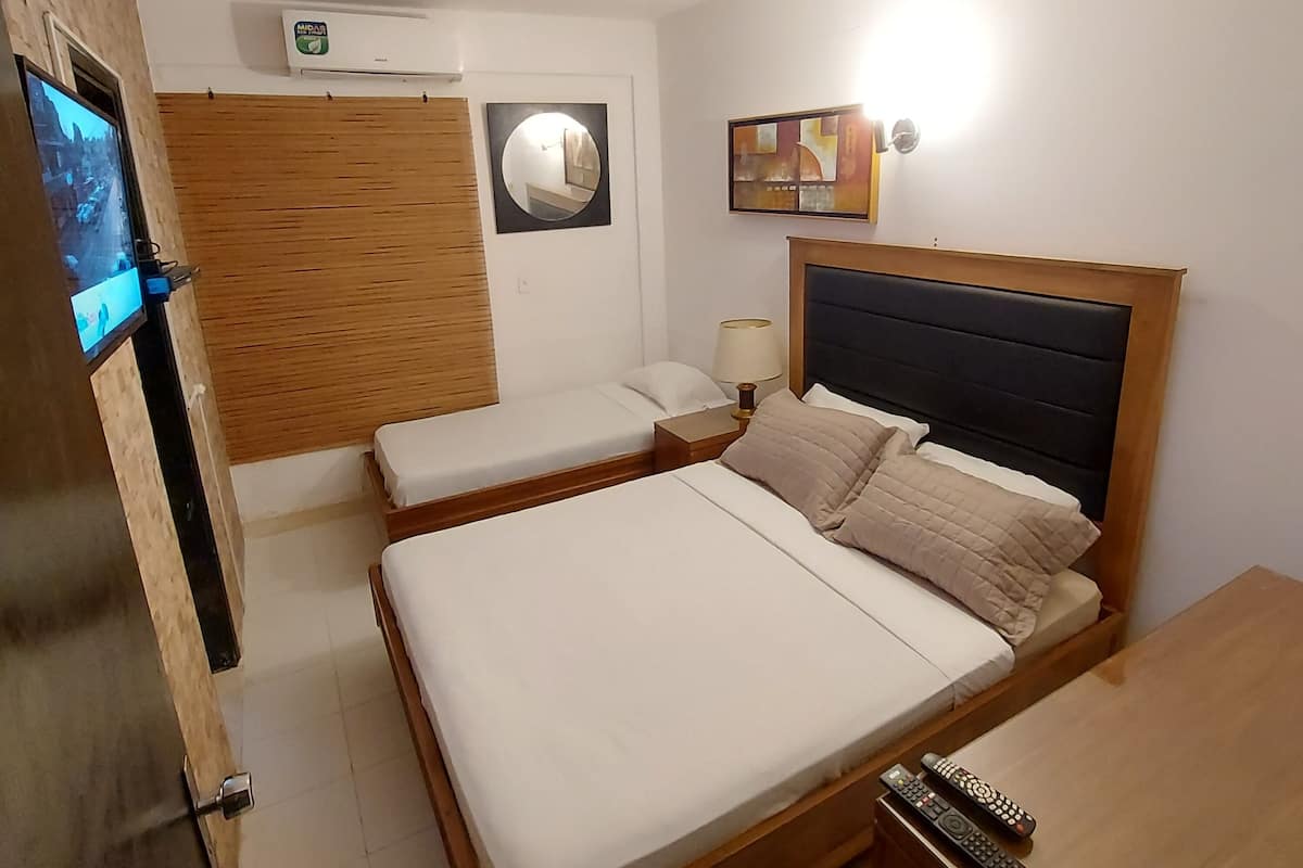 A hotel room with two beds, a TV, a wall-mounted air conditioner, a bedside lamp, and a painting.