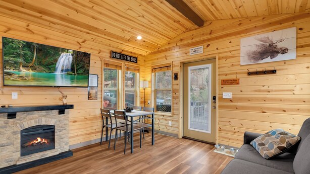 A wooden cabin interior with a fireplace, dining area, and a large window overlooking a forest. - Mt Lemmon Hotel Cabin 5 - studio cabin in peaceful Summerhaven, Arizona (Summerhaven)