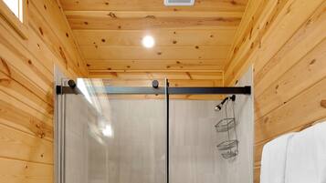 A wooden-paneled room with a glass-enclosed shower, a white towel hanging on the door, and a white countertop with cabinets.