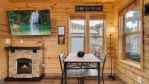 A wooden cabin interior with a fireplace, dining table, chairs, a TV mounted on the wall, and a sign above the door. - Mt Lemmon Hotel Cabin 5 - studio cabin in peaceful Summerhaven, Arizona (Summerhaven)