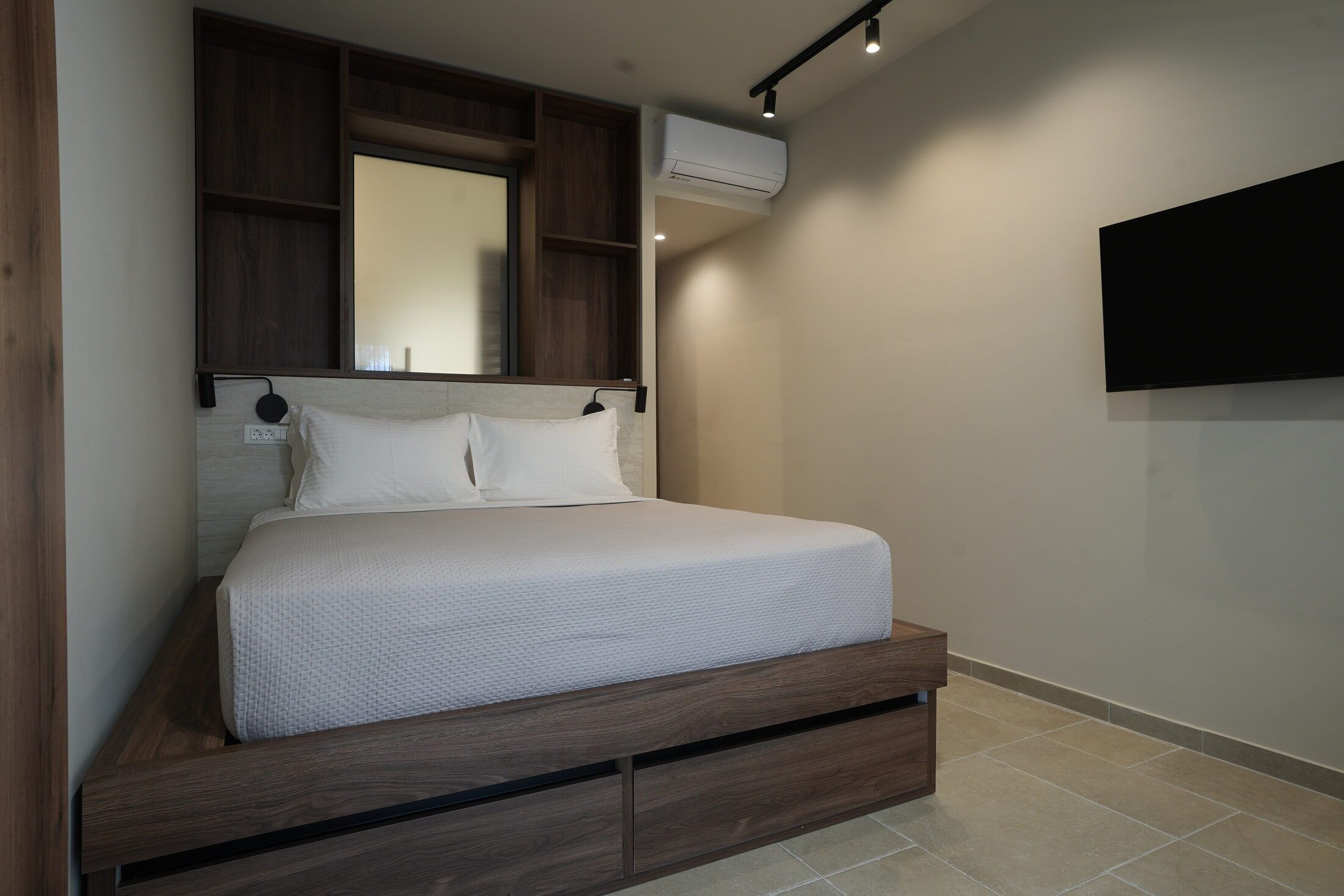 A bedroom with a bed, wooden headboard, built-in storage, an air conditioning unit, and a mounted television.