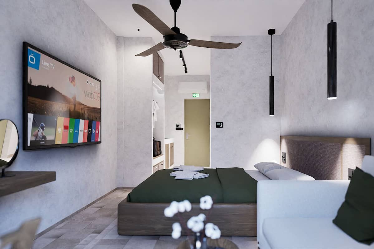 Une chambre d’hôtel moderne équipée d’un lit, d’un canapé, d’un ventilateur de plafond, d’un téléviseur fixé au mur et d’une petite table.