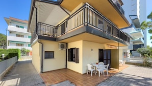 A two-story building with a balcony, a tiled patio, and a small table with chairs. - Apartment With Parking Near Center (Lignano Sabbiadoro)