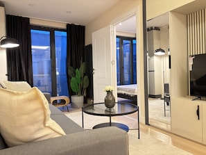Ein modernes Hotelzimmer mit Sofa, einem runden Glastisch, einem Blumentopf und einem Fernseher.