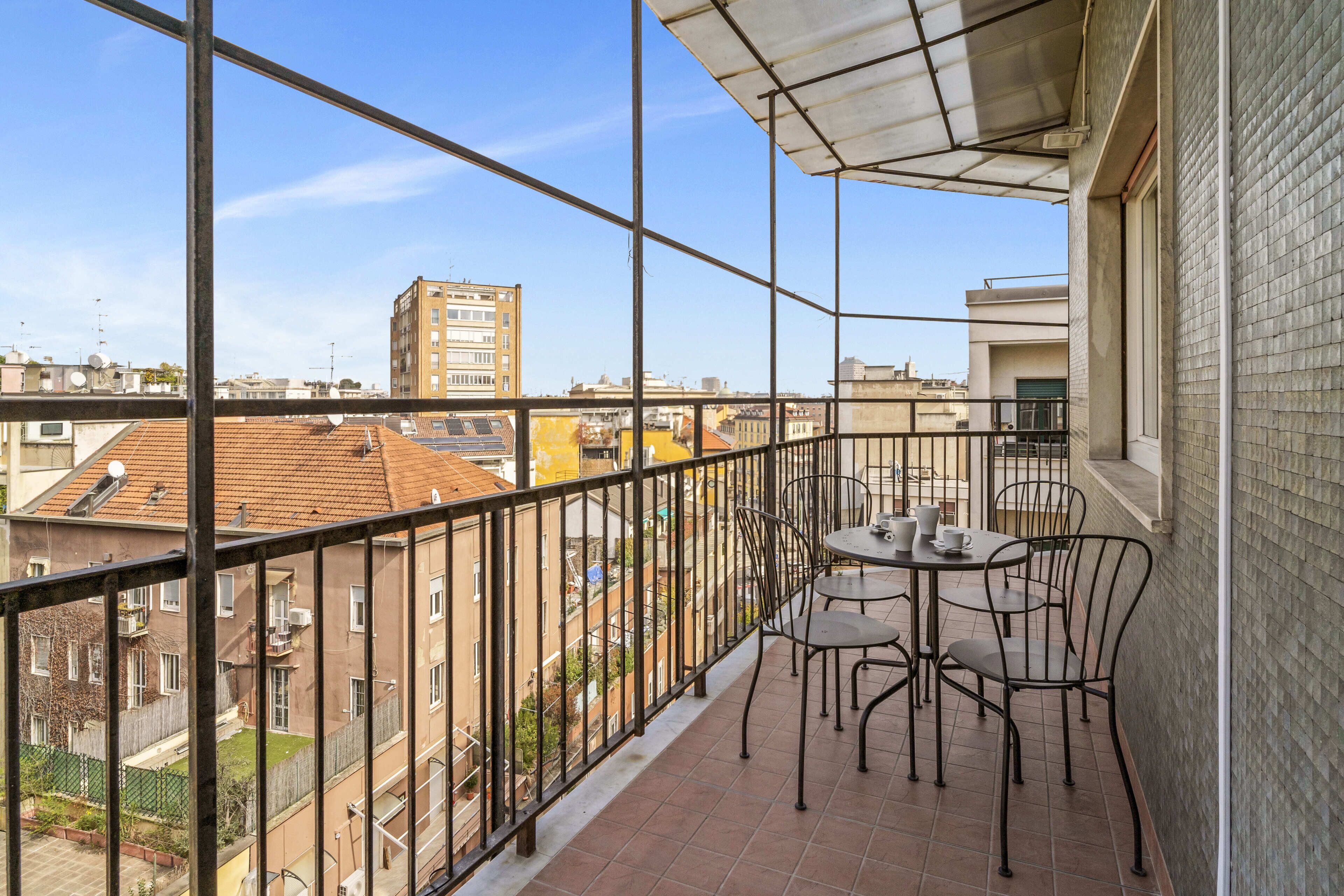 Un balcone con tavolo e sedie, vista sugli edifici circostanti e ringhiera metallica.