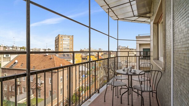 Ein Balkon mit Tisch und Stühlen, Blick auf umliegende Gebäude und einem Metallgeländer.