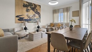 Ein modernes Wohnzimmer mit einer Sofagarnitur, einem Esstisch und einem großen abstrakten Gemälde an der Wand.