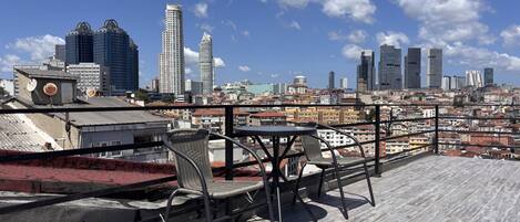 Una terraza en la azotea con vistas a un horizonte urbano, con edificios altos y un cielo despejado.