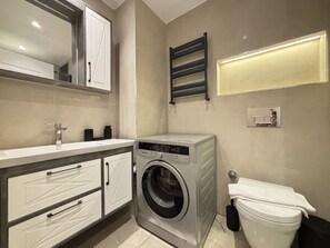 A compact bathroom with a washing machine, a toilet, a sink, and a mirror. - Chic & Cozy 2BR – Nişantaşı (Istanbul)