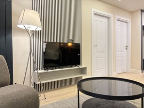 Ein modernes Wohnzimmer mit Fernseher, rundem Glastisch und einer gestreiften Wand.