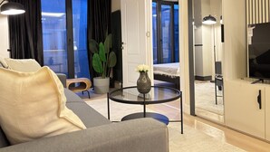 Ett modernt hotellrum med en soffa, ett runt glasbord, en krukväxt och en tv.