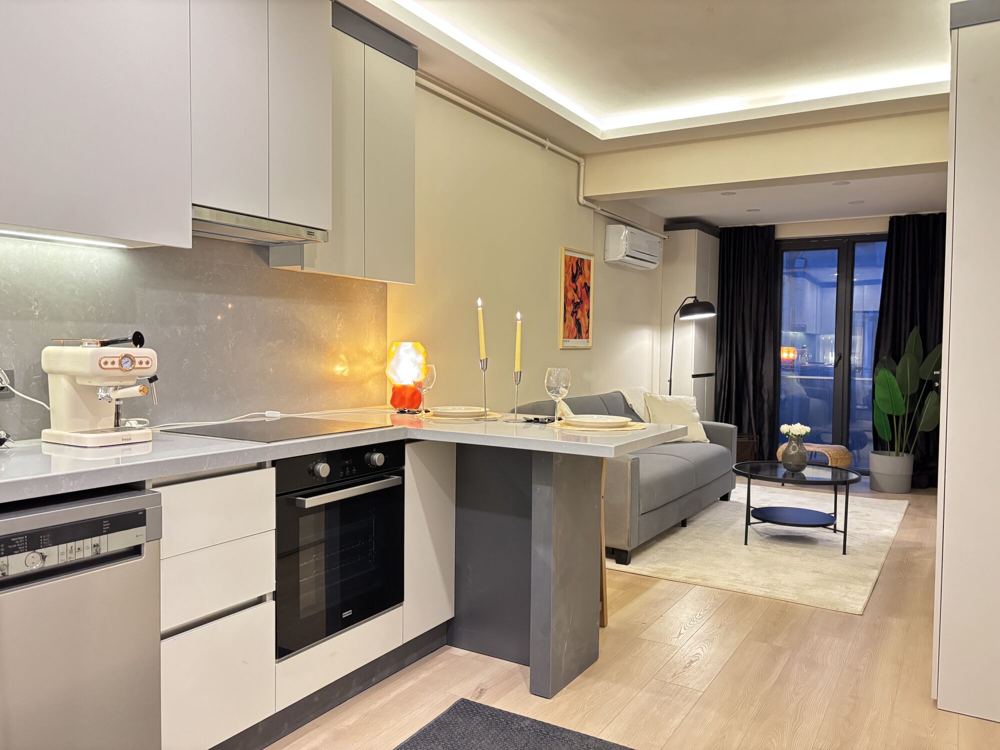 A modern kitchen with a built-in oven, a coffee machine, and a dining area with a table and chairs.