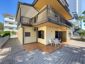 Ein zweistöckiges Gebäude mit einem Balkon, einer gefliesten Terrasse und einer kleinen Sitzgelegenheit im Freien.