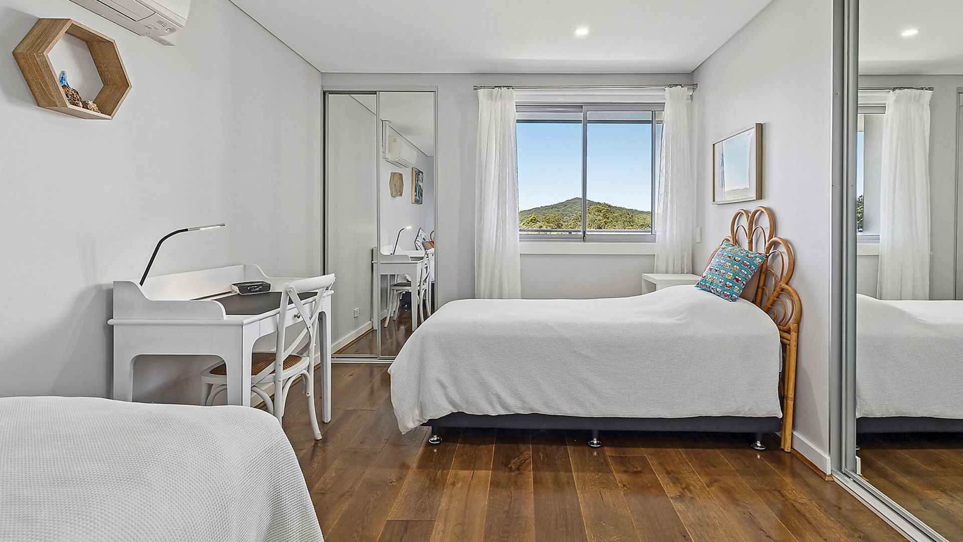 A bedroom with a bed, a desk, a chair, and a window with a view of the landscape.