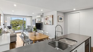 Una cocina moderna con una isla grande, un comedor con mesa y sillas, y un balcón con vistas a las colinas.