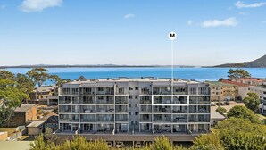 Un edificio de varios pisos con balcones, una asta de bandera y vista al mar.
