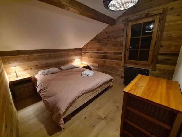 Un dormitorio de cabaña rústica con una cama individual, una mesita de noche, una pequeña mesa y un ventanal.