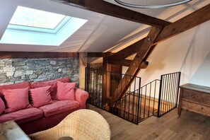 Une chambre à coucher aménagée dans un espace de type « loft », avec une lucarne, un mur en pierre, un escalier en bois et un canapé rouge.