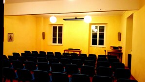 A conference room with rows of chairs, two windows, a table, and a projector screen. - CASA DEL PELLEGRINO (Ceranesi)