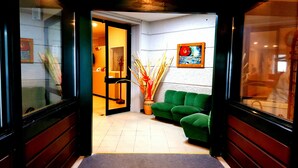 A hotel lobby with a green sofa, a vase with tall plants, and a painting on the wall. - CASA DEL PELLEGRINO (Ceranesi)